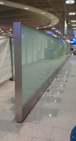 Flughafen Frankfurt, Ankunftsbereich, Sichtschutz aus Glas mit matter Folie, eingespannt in einer Stahl-Unterkonstruktion mit umlaufendem Edelstahlrahmen und Edelstahl-Blendleisten im Fußpunkt